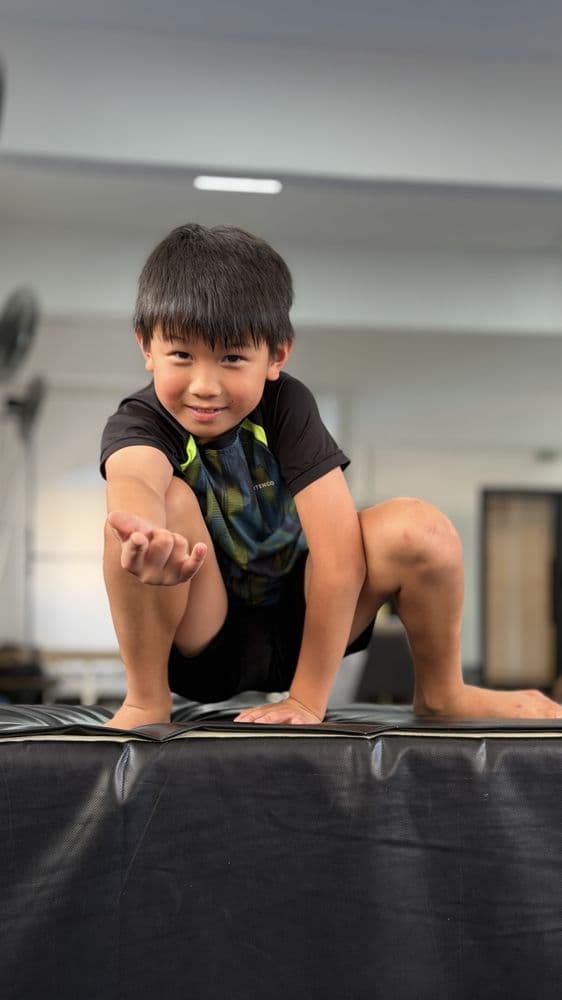 Young student smiling and reaching toward the camera on a soft mat