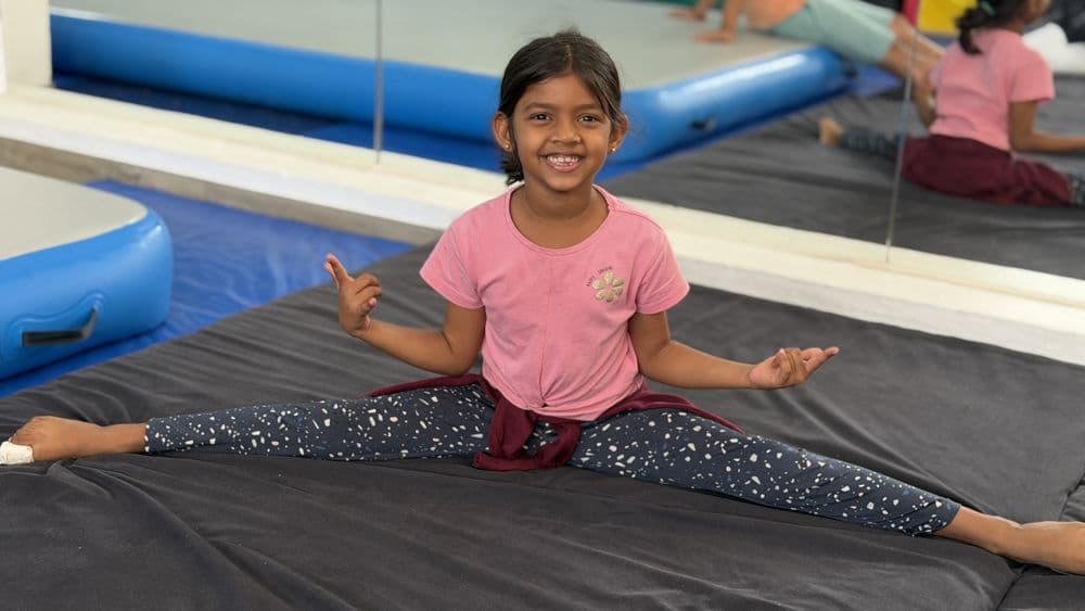 Smiling girl in a split on soft training mats